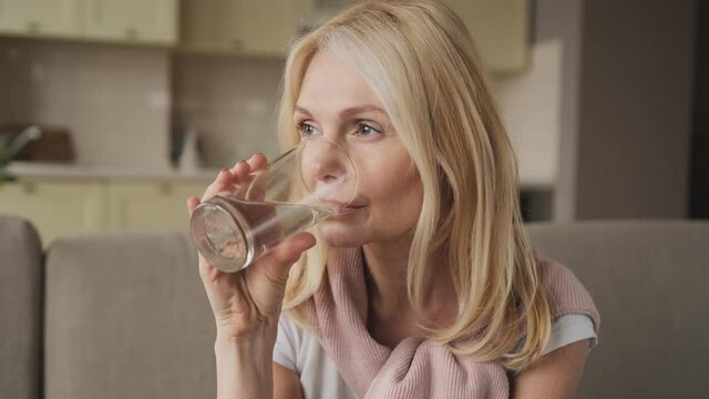 Beautiful middle aged woman drinking water ifrom a glass. Woman's face close up