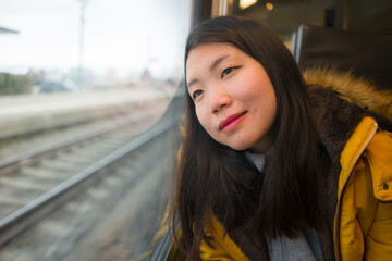Obraz premium young beautiful and happy Asian Chinese woman sitting on train looking out to window enjoying holidays travel in Europe smiling thoughtful and sweet