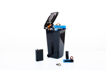 The trash can is filled with various used batteries. Defective batteries. Angle view.