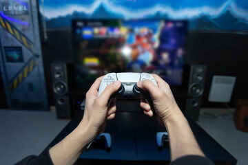 Close up of man hands holding wireless joysticks on foreground. Modern TV set with console. © Studio Peace