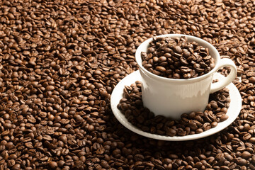 Coffee cup filled with coffee beans on a table with scattered coffee beans.