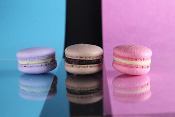 Obraz na płótnie Canvas Three macaroons on a blue black pink background different colors different tastes with place for text and reflection
