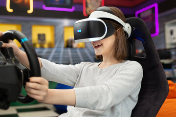 Teenage girl wearing virtual reality glasses, who holds on to the steering wheel and plays a...