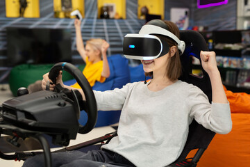Teenage girl in virtual reality glasses holds the steering wheel and plays a computer game on the...