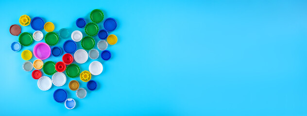 Banner with heart made of colorful plastic bottle caps on a blue background, collecting plastic for recycling and reuse.