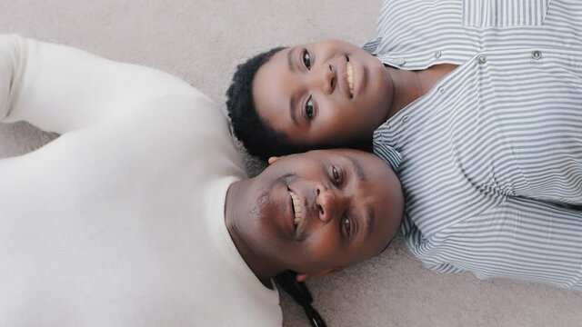 Top view of afro american couple black middle aged adult husband and ethnic wife lying together on floor looking at camera smiling sincerely, close up happy faces of african mature man and young woman