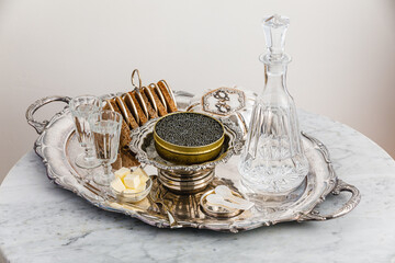 Black caviar on ice in silver bowl, Vodka and bread on white marble table