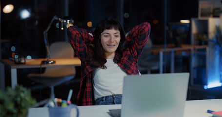 Joyful caucasian office woman doing computer project on laptop finishing work relaxing in chair...