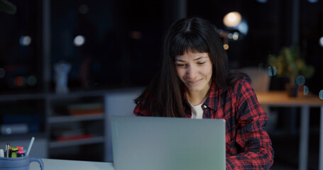 Cheerfull emotional young woman engaged in business working late at office reading news celebrating...