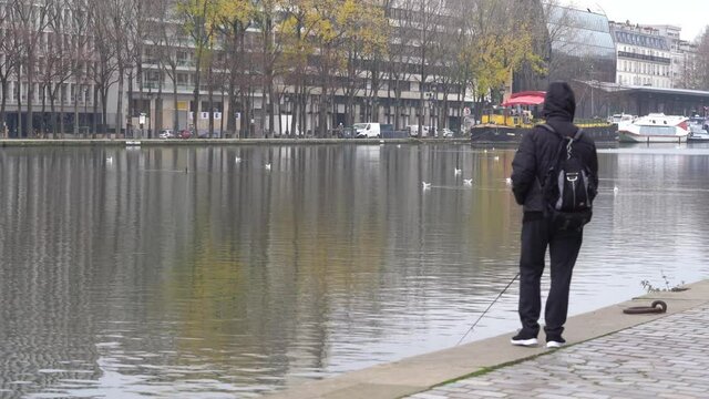 Rear view, a man is fishing in Paris canal during the winter on a cold day