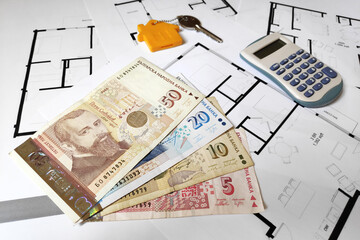 Close-up on some Bulgarian lev banknotes, a home key and a calculator on the top of building plans.