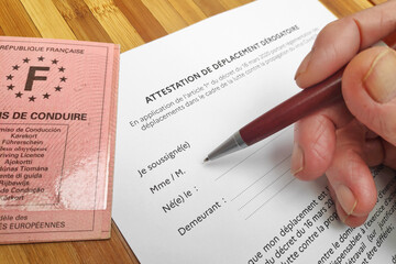 Close-up on a senior's hand filling an "Attestation de déplacement dérogatoire" that every French citizen must filled before leaving home because of the Covid-19 pandemic plan.