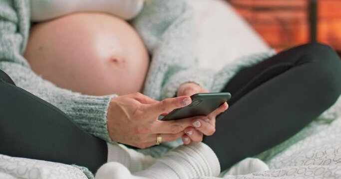 Expecting woman texting on mobile phone while relaxing on bed at home. Pregnant beautiful lady using mobile app