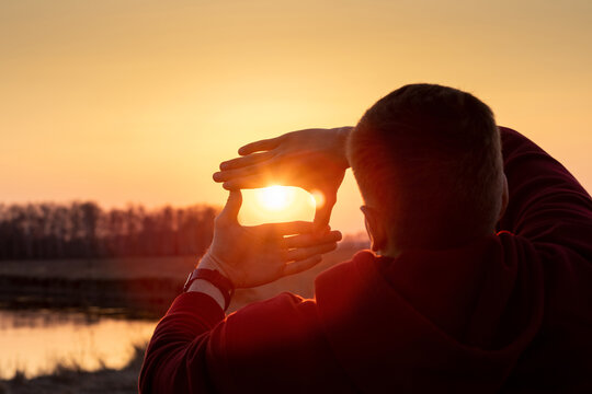 Man with his hands shows a cropping gesture composition on the background of a sunny sunset.