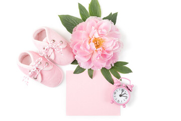 Pink baby girl shoes with peony flower, alarm clock and a blank card for message on a white background. Newborn greeting card or invitation. Copy space. Flat lay.