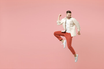 Fototapeta na wymiar Full length young happy overjoyed fun trendy fashionable caucasian man 20s in jacket white t-shirt jump do winner gesture clench fist celebrating isolated on pastel pink background studio portrait