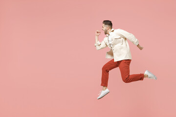 Fototapeta na wymiar Full length side profile view of young happy fun trendy sporty caucasian man wearing jacket white t-shirt jumping high run fast hurrying up isolated on pastel pink color background studio portrait