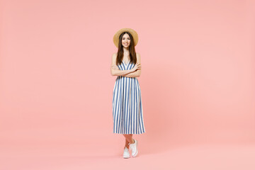 Full length young fun smiling cheerful caucasian woman in summer clothes striped dress straw hat hold hands crossed folded isolated on pastel pink background studio portrait. People lifestyle concept.