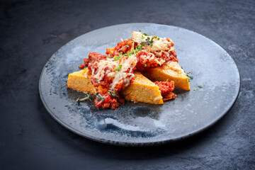 Modern style traditional Italian polenta alla sarda con salsiccia with meat sausage served as close-up on a Nordic design plate with copy space