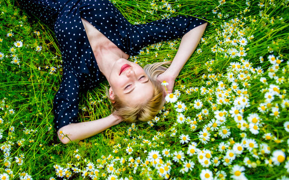 Above view at blonde woman in black dress lying in countryside chamomiles flowers meadow
