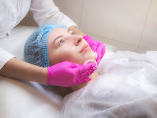 Obraz na płótnie Canvas Professional cosmetologist is cleansing skin with pads. Hands in pink gloves of beautician and caucasian woman close up. Cleaning stage. Facial skin care. Beauty salon, cosmetology clinic, spa.