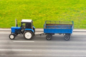 Blue tractor with a trailer driving on the highway.