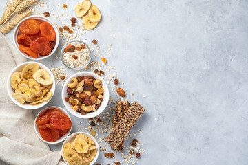 Fototapeta premium Healthy, vitamin-rich, sweet snacks. Banana chips, dried apricots, different types of nuts, raisins and granola bar on a gray background.