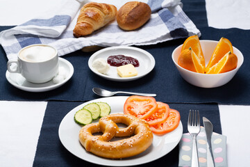 Pretzel breakfast served with cucumber, tomato, orange, croissant, bread and coffee