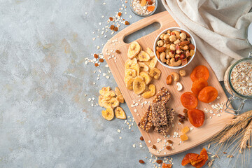 Vitamin-rich, healthy natural sweets on a gray background. Granola bar, nuts and dried fruits on a wooden board.