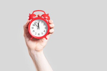 Analog red alarm clock in hand on a white background.