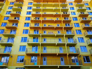 Facade of new yellow color residential building. Rising prices for purchase, sale and rental of real estate. Inexpensive apartments. Comfortable housing. Cityscape. City living. Windows and balcony