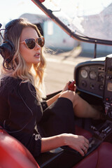 Young fashionable woman pilot in headset ready to fly in small red airplane. Beautiful life,...