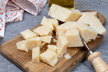Parmesan cheese cut into pieces on wooden cutting board. Italian cheese in close-up.