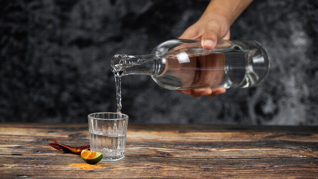Bebida mexicana de agave mezcal tipo tequila hecha en oaxaca servida en veladora oaxaque&ntilde;a sobre mesa de madera r&uacute;stica acompa&ntilde;ada de lim&oacute;n y sal de gusano 