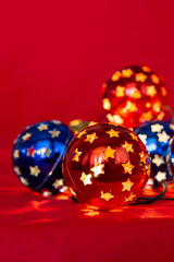Decorative Christmas glowing garland lights multi-colored balls with star shaped holes. Red and blue balls on a red background, festive vertical photo 