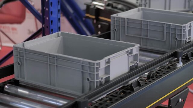 Empty grey plastic crate boxes, containers moving on conveyor belt at package exhibition, trade show - close up view. Industrial, equipment, technology concept
