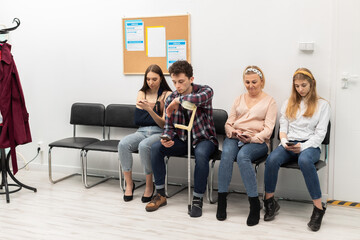 Obraz na płótnie Canvas Patients sit in a clinic waiting for their turn to go to the doctor's office. They look at their cell phone while waiting.