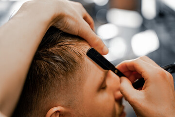 Haircut and personal care, a man in a barbershop receives hair cutting services, a master shaves his hair with a blade