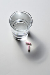 a glass beaker and two pink capsules with vitamins. close-up.