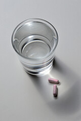 a glass beaker and two pink capsules with vitamins. close-up.