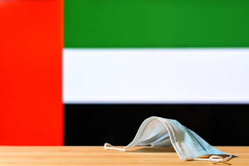 A medical mask lies on the table against the background of the flag of UAE. The concept of a mandatory mask regime for residents of the country and tourists in UAE a pandemic.