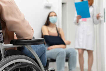 In the foreground a wheelchair and in the background a redheaded doctor standing next to her...