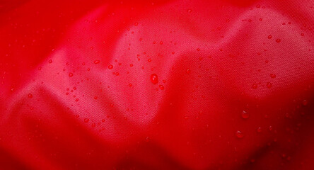 Large drops of water on a red textile with a waterproof effect. Water-repellent impregnation....
