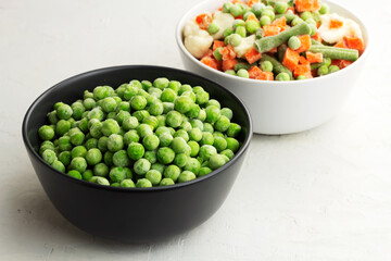 Frozen green peas in a grey bowl on light background