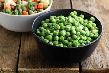 Frozen green peas in a grey bowl on wooden background