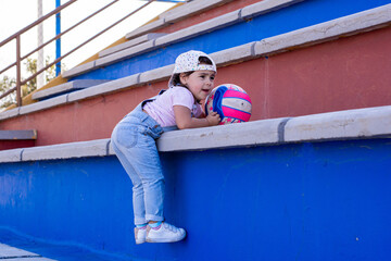 Two-year-old girl hanging from some stairs where she was climbing with her ball.