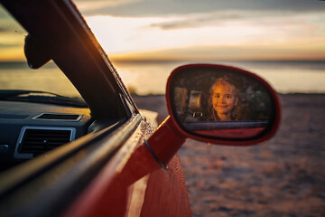 Autumn road trip, freedom and family traveler. Pretty girl sitting in the car on the bank of sea, rest and leisure, looking at beautiful sunset after rain, drops on windshield, fall outdoor lifestyle