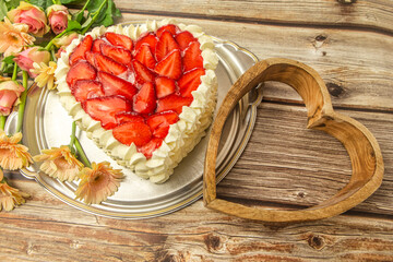 Close-up of a delicious heart shaped strawberry cake on a wooden background in a lovely arrangement with a wooden heart and flowers. Birthday, valentines and mothers day concept