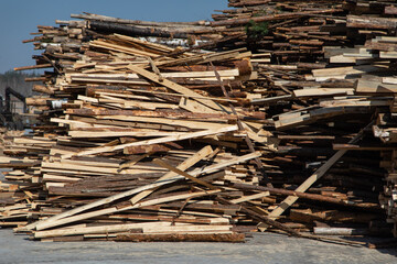 A cord of cut birch wood for firewood piled high under a blue sky with white clouds. The long logs have been cut with a chainsaw from a forest and stacked. They are ready for harvest and logging.