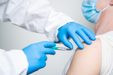 A doctor dressed in a protective suit vaccinates a patient against coronavirus.